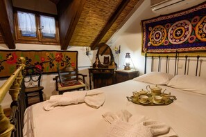 A traditional room with a bed, a wooden chair, a small table with a teapot and cups, and a colorful tapestry on the wall.