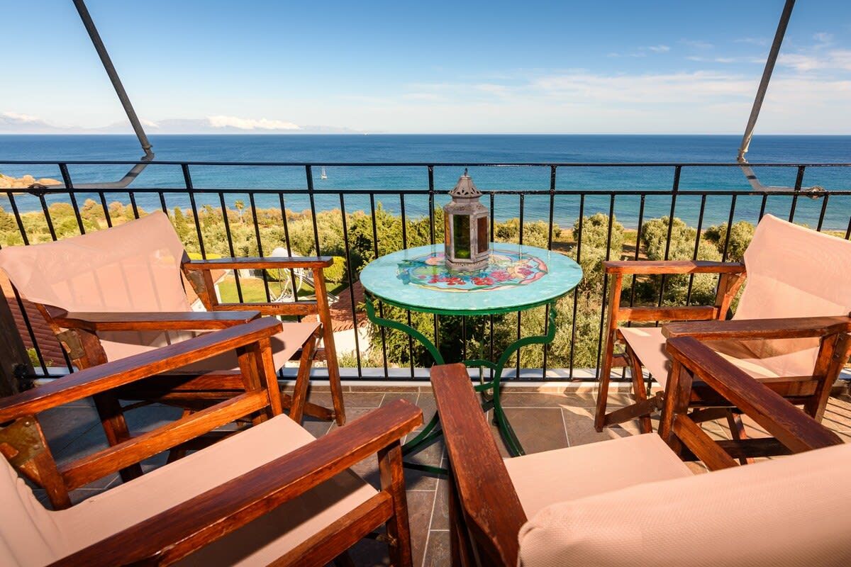 A balcony with wooden furniture and a table with a decorative centerpiece, overlooking a coastal view.
