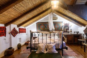 A room with a high ceiling, a bed with a canopy, a sewing machine, and traditional textiles on the walls.