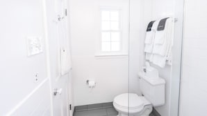 Un baño pequeño y blanco con un inodoro, una ventana y un perchero para toallas.
