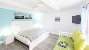 Un dormitorio con cama, mesitas de noche, ventilador de techo, televisor y obras de arte en la pared.