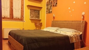 Ein Zimmer mit einem Bett, einem Sessel, einem kleinen Tisch und einer Wand mit einem Bild und einem Regal.