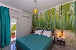 A bedroom with a bed, a nightstand, a wall-mounted lamp, a window with curtains, and a bamboo forest mural. - Spyros apartment 2 in Platanes Rethymno (Platanes)