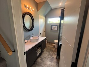 A modern bathroom with a vanity, sink, and mirror. There is a framed picture on the wall and a window providing natural light. - Modern 3 bedroom luxury retreat! Wine bar, upper deck, lower patio! (Penticton)