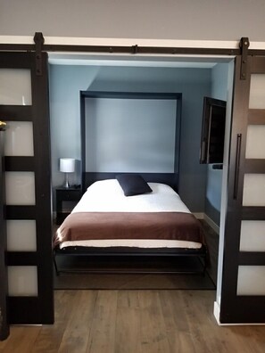 A bedroom with a bed, a nightstand, a lamp, and a television. - Modern 3 bedroom luxury retreat! Wine bar, upper deck, lower patio! (Penticton)