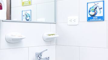 A bathroom with a sink, mirror, and two soap dispensers. There are two signs on the wall promoting water conservation.
