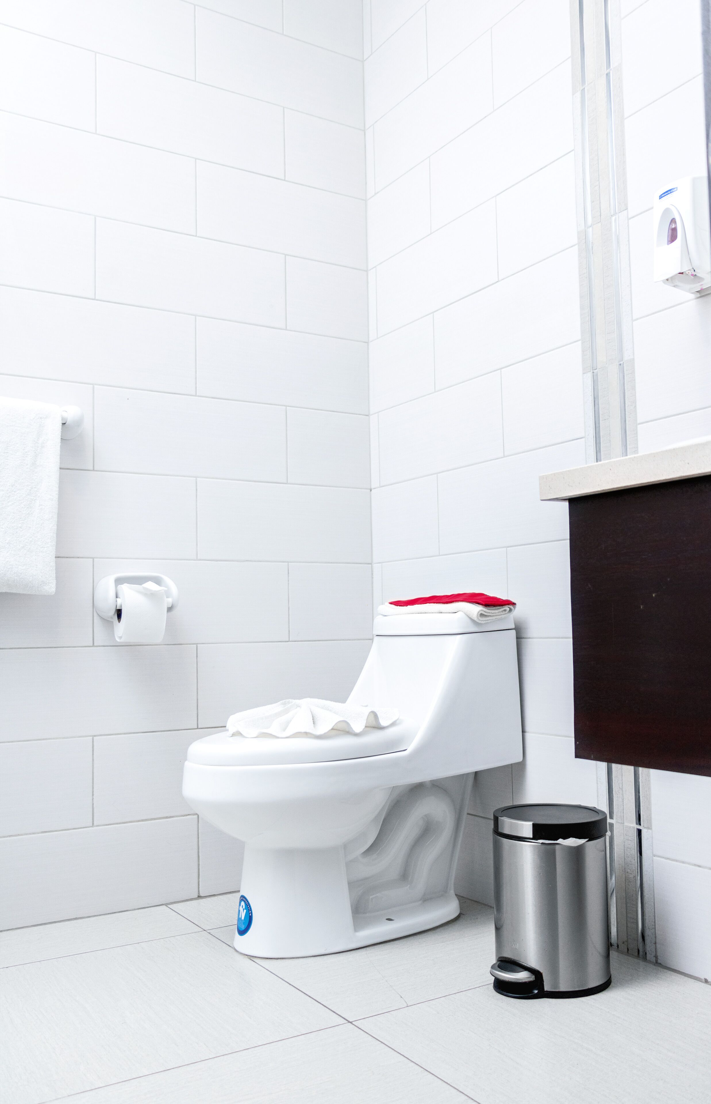 Un baño moderno con azulejos blancos, un inodoro blanco, un cubo de basura plateado y un perchero para toallas.