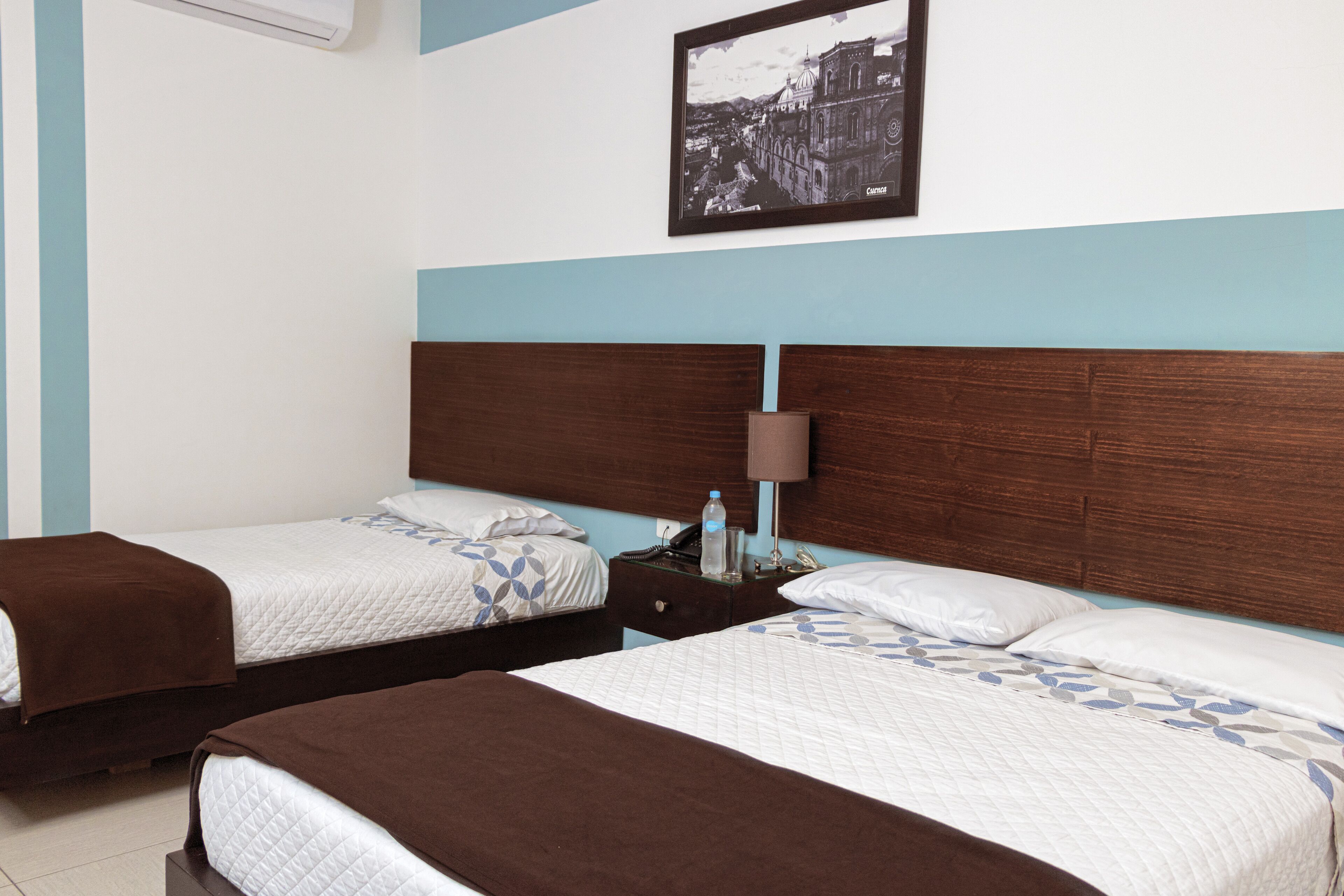 A hotel room with two beds, a nightstand, a lamp, and a framed picture on the wall.