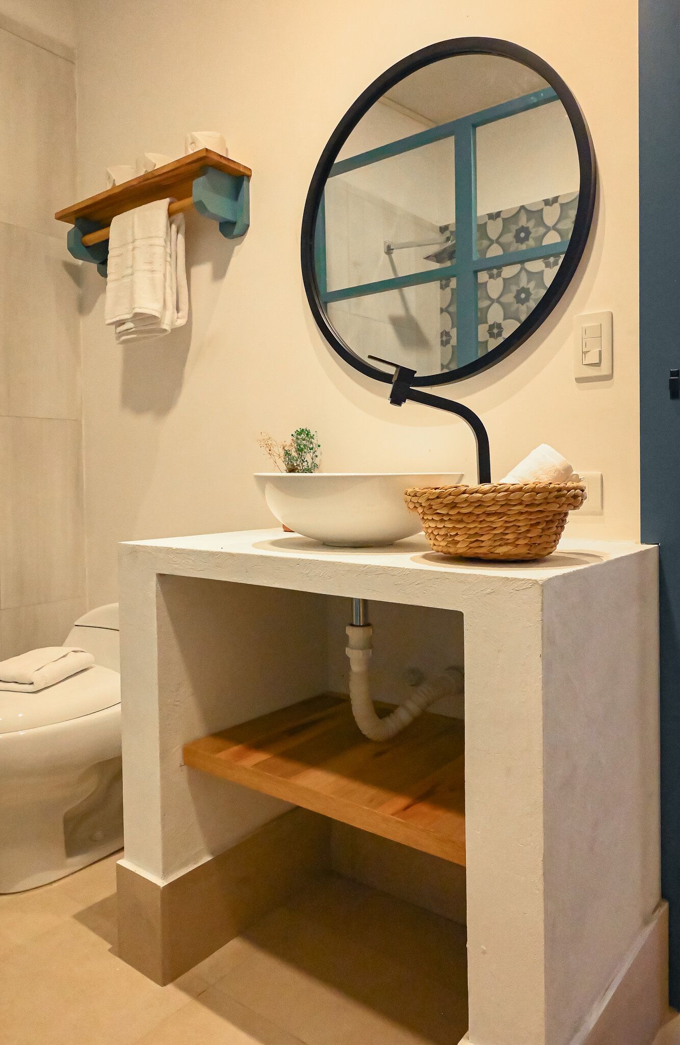 A bathroom with a white sink, a round mirror, a small plant, and a towel rack.