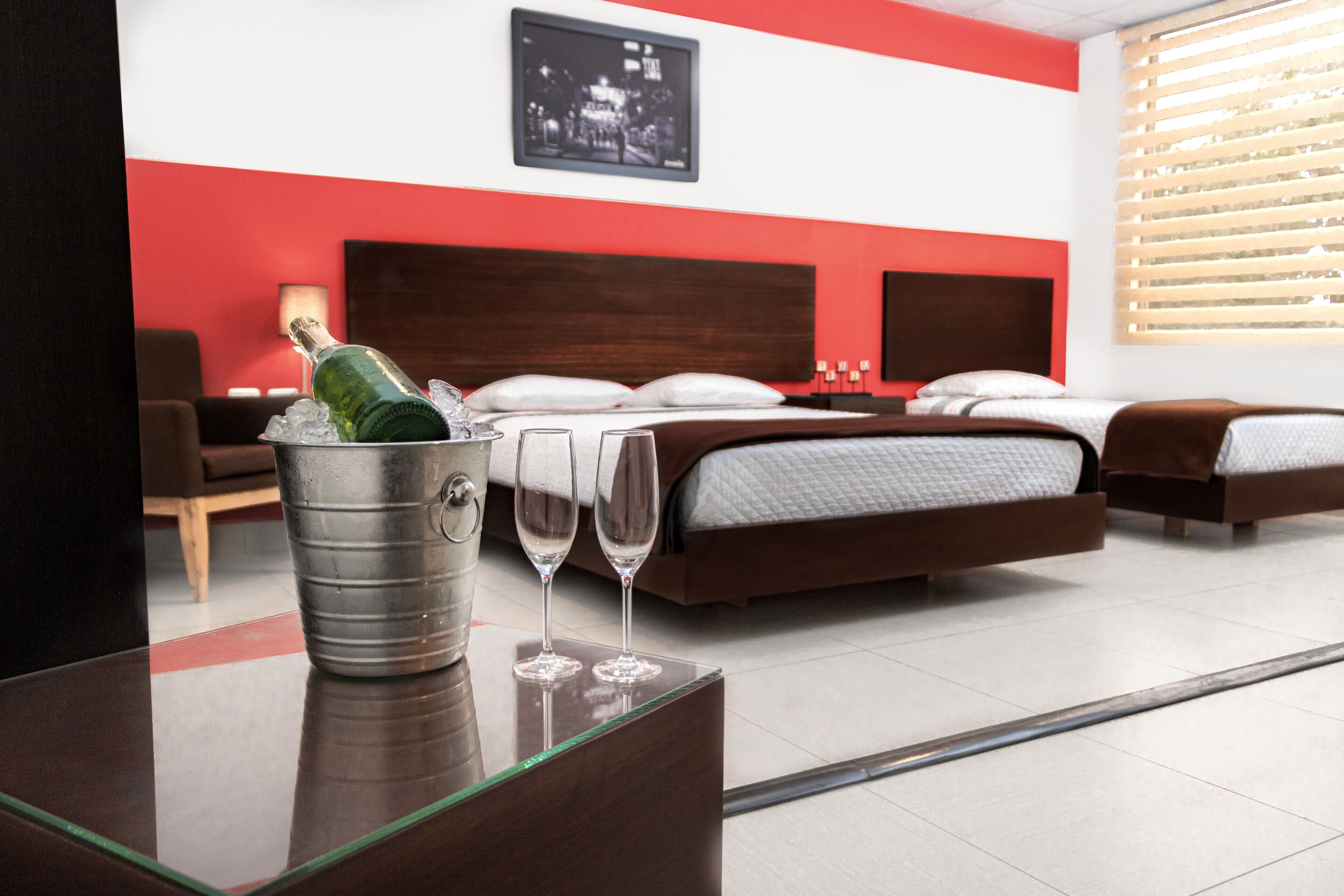 Un cuarto de hotel con cama, mesitas de noche, lámpara y un cuadro en la pared.