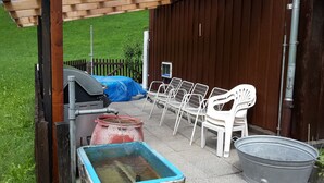 En uteplats med en grill, vita plaststolar, en blå och röd tunna och en metallhink.