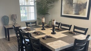 A dining room with a rectangular table, black chairs, a vase, a lamp, and a large window with blinds. - South Facing Pool, Near Disney, 5 Bed Luxury (Kissimmee)