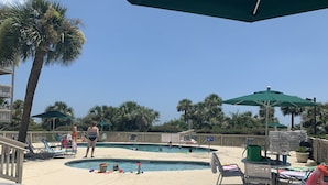 Área de piscina com espreguiçadeiras, guarda-sóis e um deck de madeira.