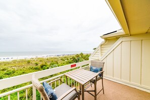Ein Balkon mit Blick auf den Strand, ein Tisch und zwei Stühle.