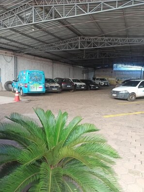A covered parking area with multiple vehicles, including a blue van and several cars, and a potted plant in the foreground. - Borges Hotel (Imperatriz)