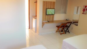 A room with a bed, a desk with a chair, a television, and a window with blinds.