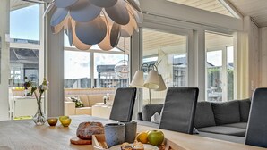A modern living room with a wooden table, grey sofas, and a large window offering a view of the city. - 2 bedroom beach front home in Rønde (Rønde)