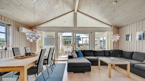A spacious living area with a high ceiling, wooden walls, a large sofa, a coffee table, and a dining table with chairs. - 2 bedroom beach front home in Rønde (Rønde)