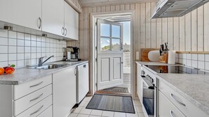 A narrow kitchen with white cabinets, a coffee maker, and a view through a door. - 2 bedroom beach front home in Rønde (Rønde)