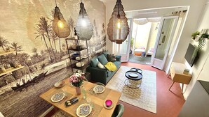 A dining area with a wooden table set for two, a green sofa, and hanging pendant lights. - Dar Saad a hanging garden in the historic center of Aix  (Aix-en-Provence)