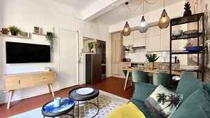 A modern living room with a flat-screen TV, a sofa, a coffee table, and a dining area with a kitchen in the background. - Dar Saad a hanging garden in the historic center of Aix  (Aix-en-Provence)