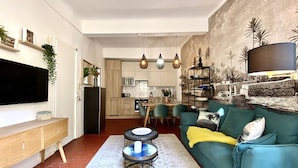 A modern living room with a teal sofa, a coffee table, and a dining area with chairs and a table. - Dar Saad a hanging garden in the historic center of Aix  (Aix-en-Provence)