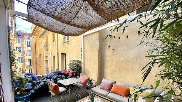 An outdoor seating area with a table, chairs, and a sofa. There are plants and flowers around, and a building is visible in the background. - Dar Saad a hanging garden in the historic center of Aix  (Aix-en-Provence)