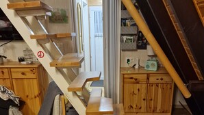 Una escalera de madera con barandilla, un área de comedor con banco y una cocina con armarios y un radio.