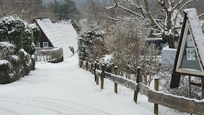 Una carretera rural cubierta de nieve con una valla de madera y una casa de techo inclinado.