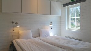 Une chambre avec deux lits, du linge de lit blanc et des lampes fixées au mur.
