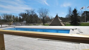 Une piscine avec une terrasse en bois, une structure en forme de tipi et des arbres en arrière-plan.