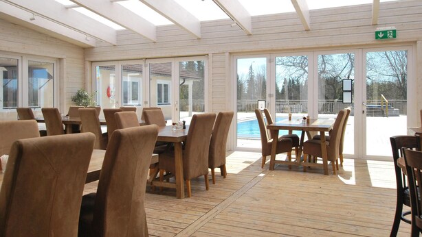 Une salle à manger baignée de lumière naturelle, avec des tables et des chaises en bois, de grandes fenêtres et une vue sur une piscine.
