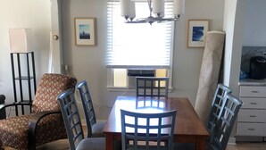 Uma área de refeições com mesa e cadeiras de madeira, um candelabro e uma janela com persianas.
