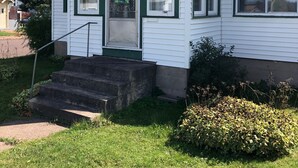 Uma casa de dois andares com varanda da frente, um pequeno lance de degraus e uma porta verde.