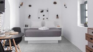 A modern, minimalist bedroom with a bed, bedside tables, a desk, and chairs. - Noelia Suites (Santorini)