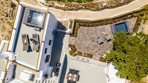 An aerial view of a rooftop terrace with a swimming pool, sun loungers, and a dining area. - Noelia Suites (Santorini)