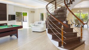 Amplia sala de estar con una escalera curva, una mesa de billar y un espacio de estar acogedor.