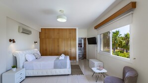 Un dormitorio moderno con una cama grande, un armario de madera, un televisor y una ventana con vistas a palmeras.