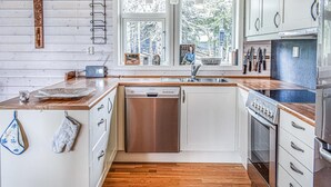 A modern kitchen with white cabinetry, a dishwasher, an oven, and a sink. There are two windows providing natural light, and a radio is visible on the counter. - Stunning home in Sjusjøen with sauna (Sjusjøen)