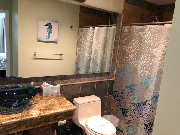 A bathroom with a granite countertop, a toilet, a seahorse painting, and a shower with a dotted curtain.