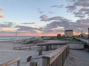 A beach with a wooden boardwalk, a signpost, and buildings in the background.