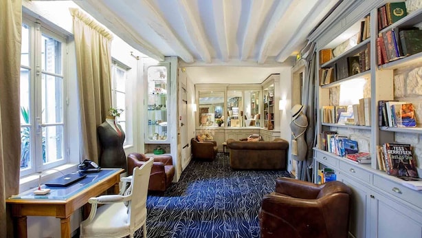 Una habitación con escritorio, sillas, sofá y estantería, además de un espejo.