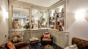 Habitación en esquina con un espejo grande, estanterías, un sillón de cuero y una pequeña mesa.