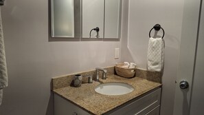 Un bagno con piano in granito, lavabo, specchio, porta asciugamani e cesto con asciugamani.