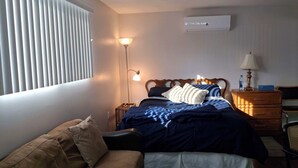 Et soveværelse med en seng, et sengebord, en lampe og et vindue med persienner.