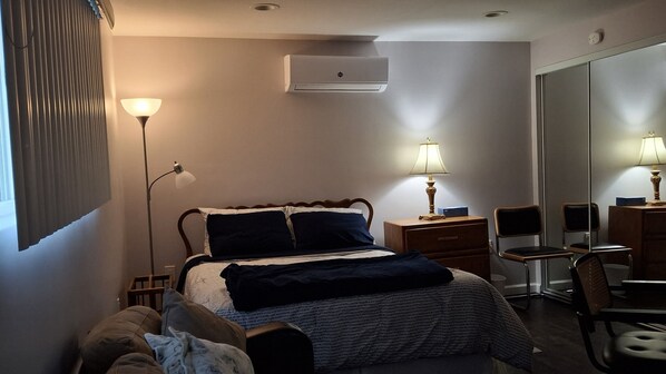Una habitación de hotel con cama, lámparas de noche, escritorio con silla, armario y aire acondicionado.