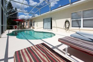 A covered outdoor swimming pool with a lounge area, a patio with a table and chairs, and a view of a house in the background. - Jay's Beach Disney Villa - South Facing Pool (Davenport)