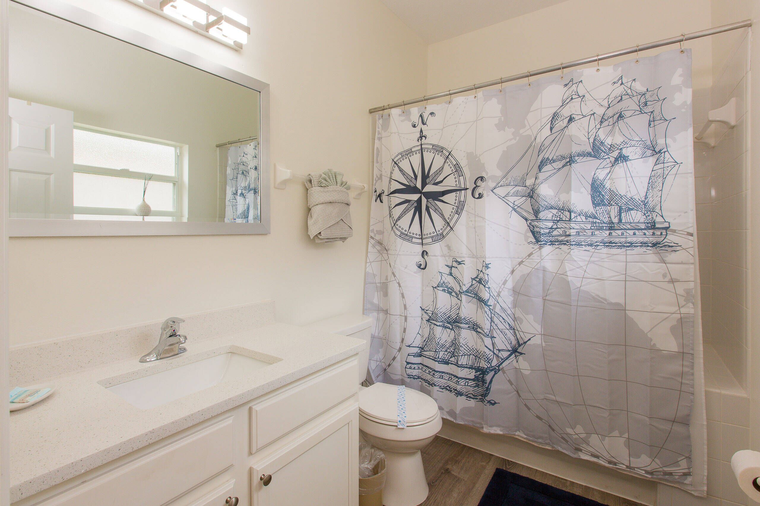 A bathroom with a white sink, mirror, and toilet. There is a shower curtain with a nautical design.