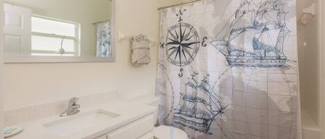 A bathroom with a white sink, mirror, and toilet. There is a shower curtain with a nautical design.
