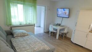 A modern, well-lit room with a grey sofa, a small white table, and a TV mounted on the wall. - Ferienwohnung in Odenthal (Odenthal)